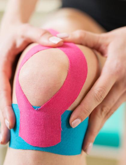 Ginocchio con nastro kinesiologico rosa e blu applicato per supporto.