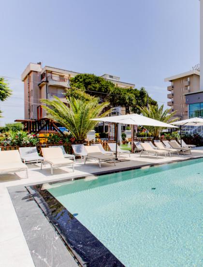 Außenpool mit Liegestühlen und Sonnenschirmen in der Nähe eines modernen Hotels.