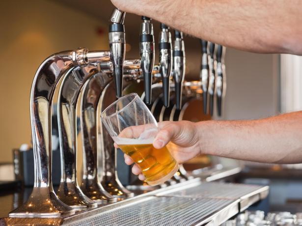 Mano che versa birra da un rubinetto in un bicchiere.