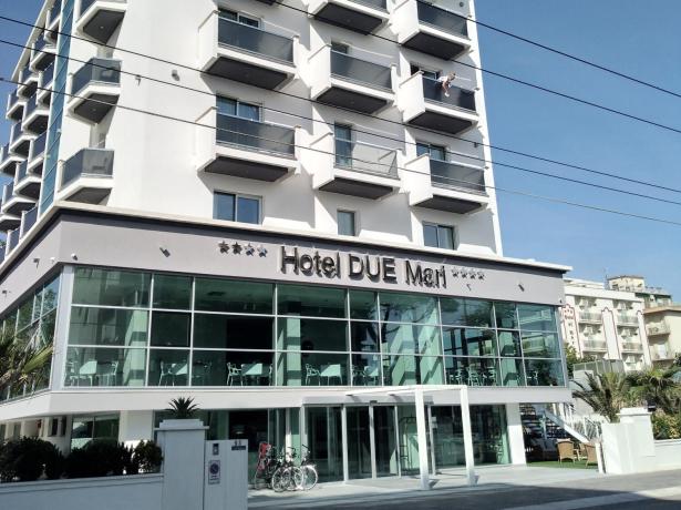 Hotel moderno con balconi e vetrate, cielo azzurro.