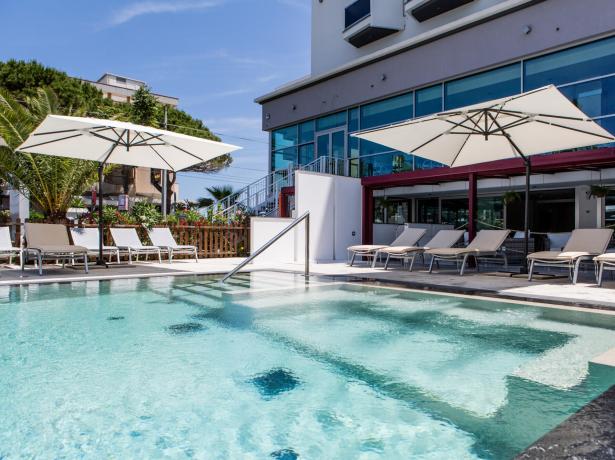 Outdoor pool with sun loungers and umbrellas near a modern hotel.