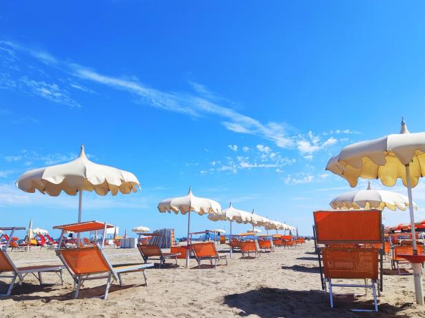 Strand mit Sonnenschirmen und Liegestühlen unter blauem Himmel.