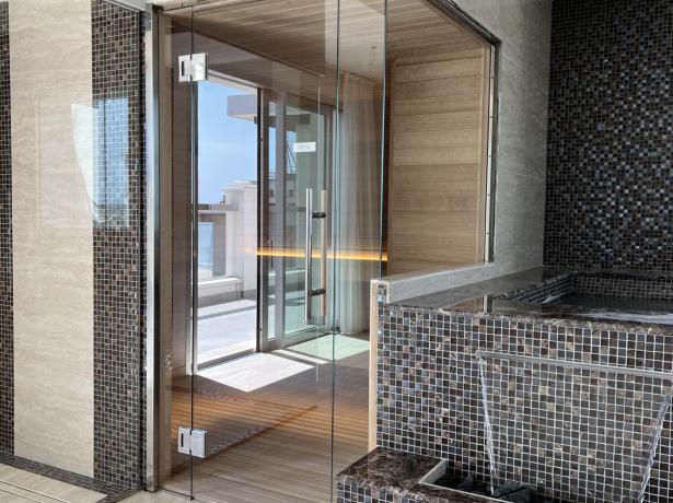 Elegante moderne Sauna mit Glaswänden und dunklen Mosaikfliesen.
