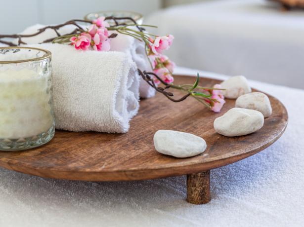 Candle, towels, and flowers on a wooden tray.