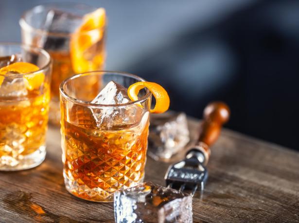 Cocktail with ice and orange peel on a wooden table.