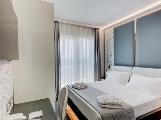 Camera moderna con letto matrimoniale, scrivania e finestra con tende.