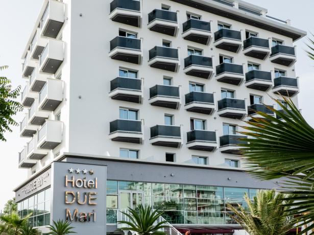 Modernes Hotel mit Balkonen, Glasfenstern und Palmen.