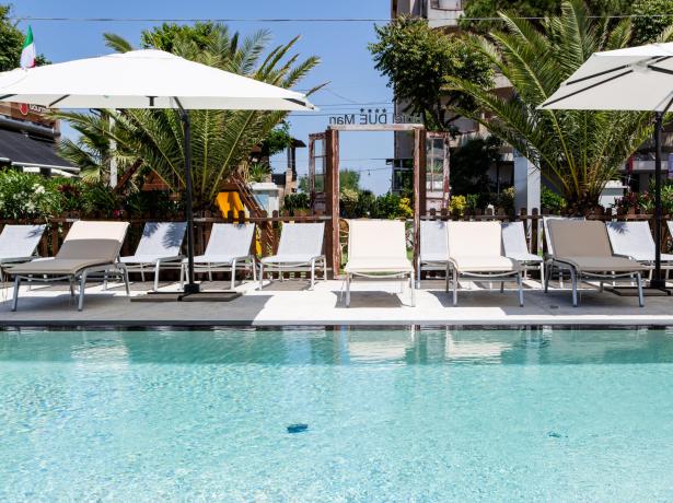 Piscina all'aperto con lettini e ombrelloni, circondata da palme.