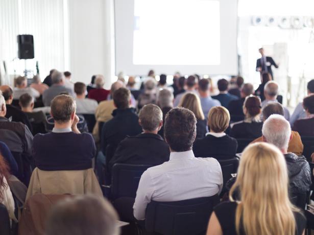 Persone sedute ascoltano una presentazione in una sala conferenze.