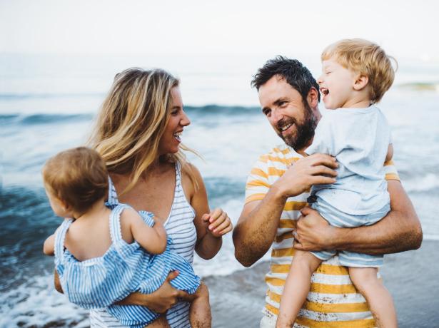 Famiglia felice in spiaggia, genitori con due bambini piccoli sorridono e giocano.