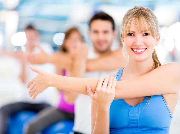 People stretching in a gym, smiling.